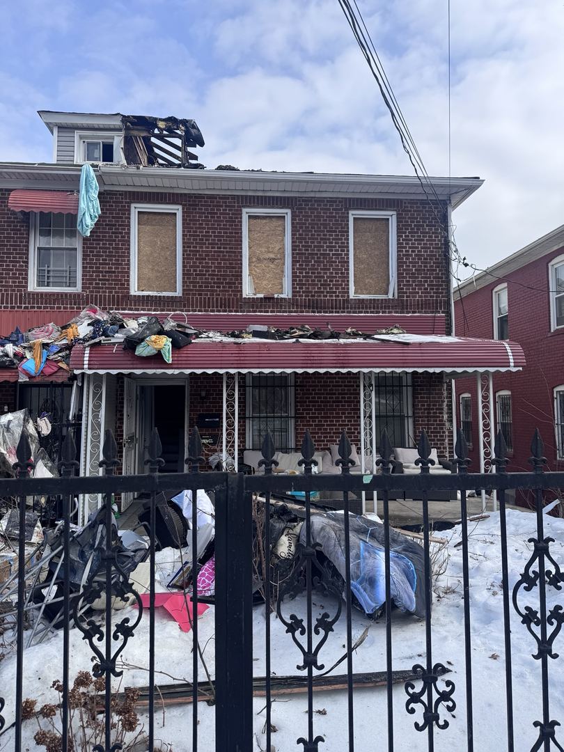 Brick home with a fire-damaged roof, exposed dormer framing, and boarded windows